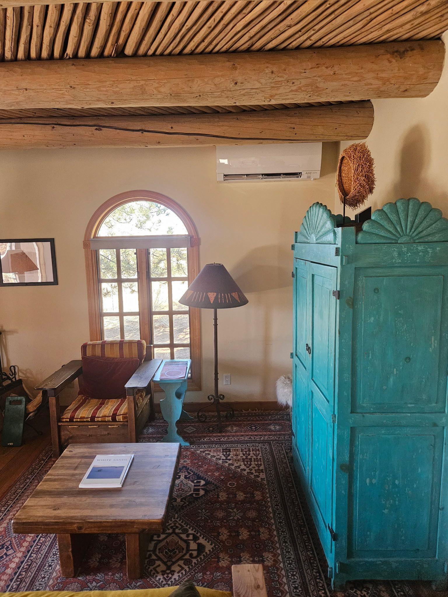 Living room with teal armoire, rustic furniture, and arched window.