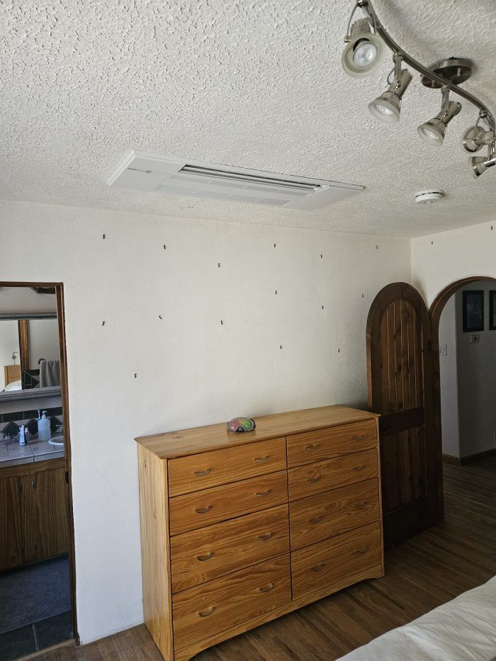 A bedroom with a wooden dresser, white walls, and a recessed ceiling light.