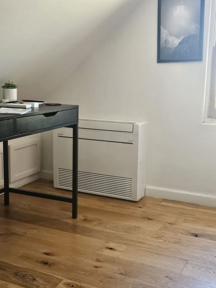A modern office corner with a desk, heater, wooden floor, and a framed picture on the wall.