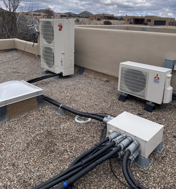 HVAC units on a rooftop. White units, black conduit, and a control box. Cloudy day, desert landscape.