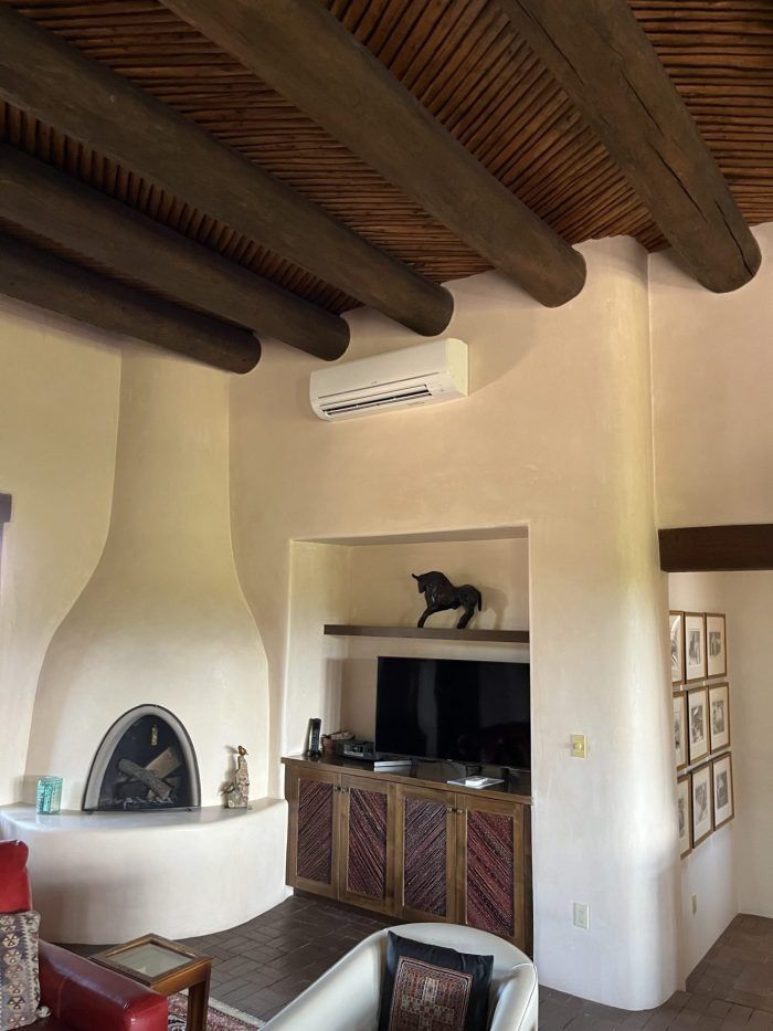 Living room with fireplace, TV, and air conditioner; rustic beams on ceiling.