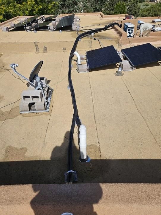 Rooftop with solar panels, black hose, satellite dish, and AC units on a sunny day.