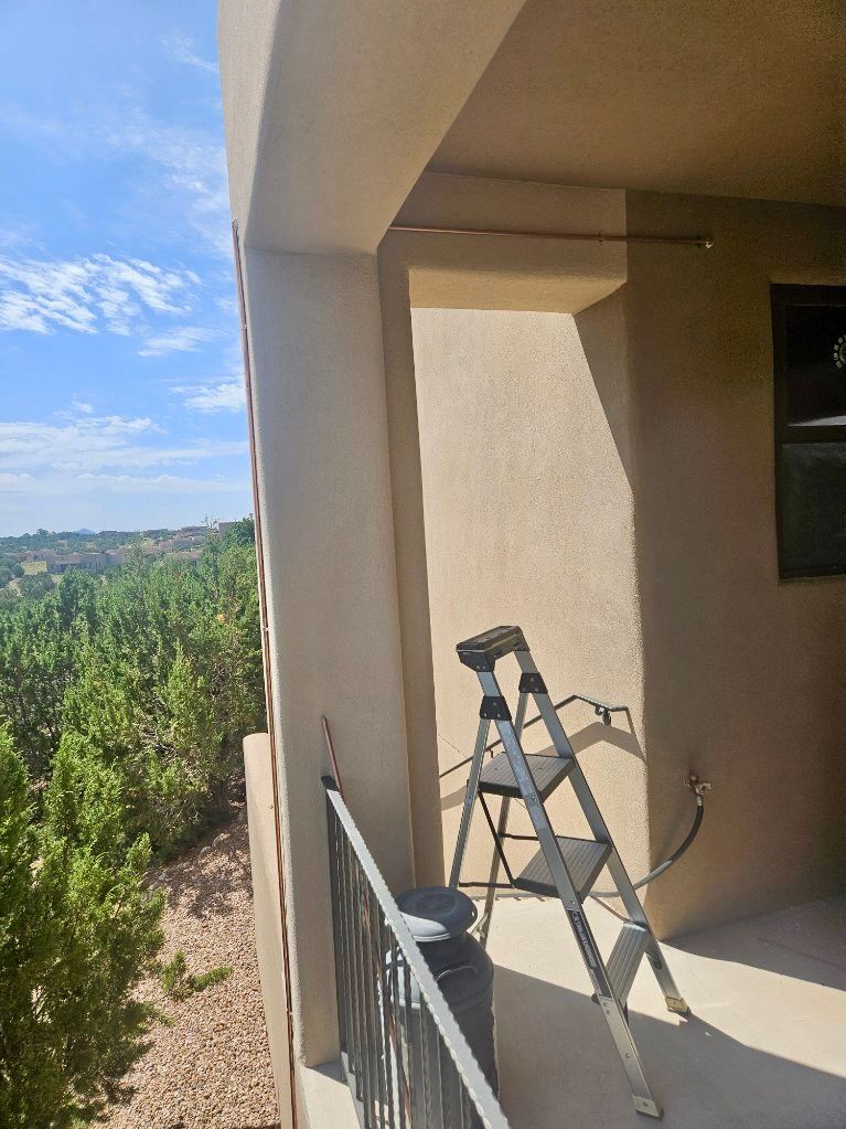 A step ladder on a balcony overlooking greenery, under a blue sky.