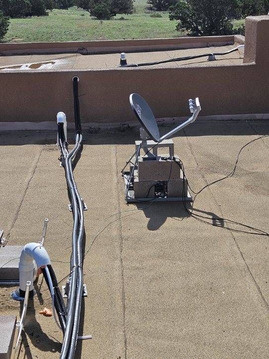 Satellite dish on a rooftop with cables and a sunny, outdoor setting.