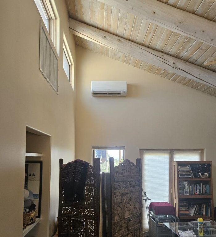 High-ceilinged room with a wall-mounted AC unit; wooden beams, windows, and decorative screen visible.