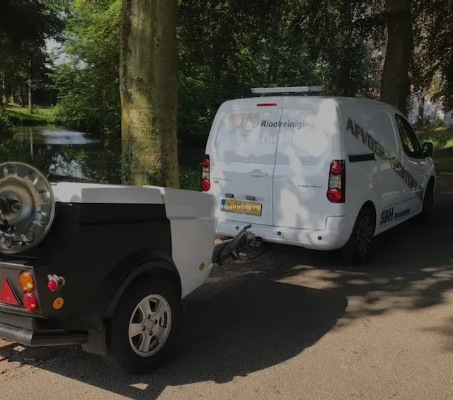 Witte bedrijfsbus van SBH Rioolreiniging met aanhanger, geparkeerd op een laan naast een vijver.