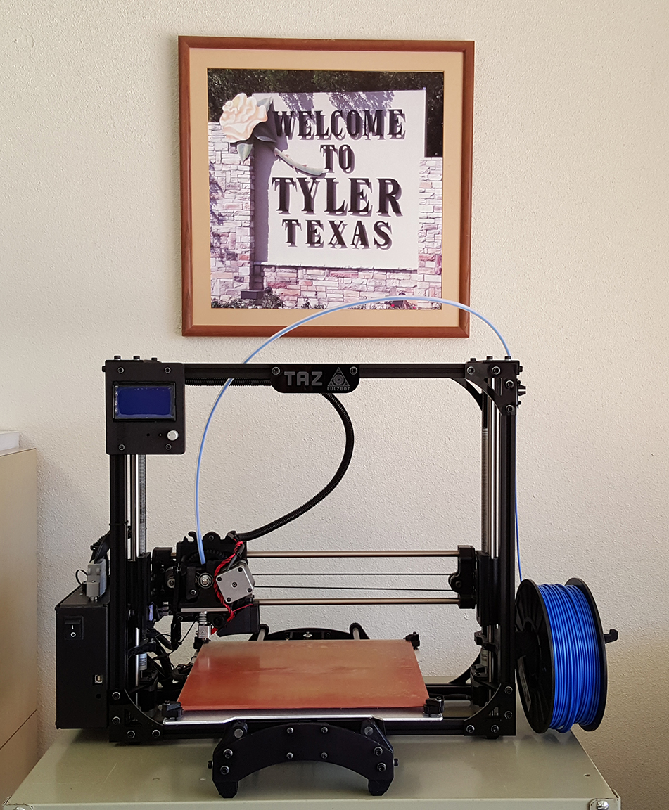 A black 3D printer with blue filament next to a framed 