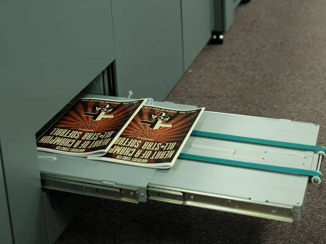 Two printed posters on a metal tray of a printing press, showing a starburst design.