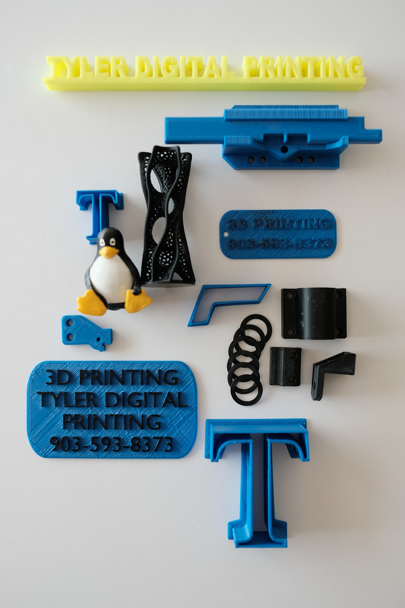 Collection of 3D-printed objects in blue, yellow, and black. Includes a penguin, logos, and various geometric shapes.