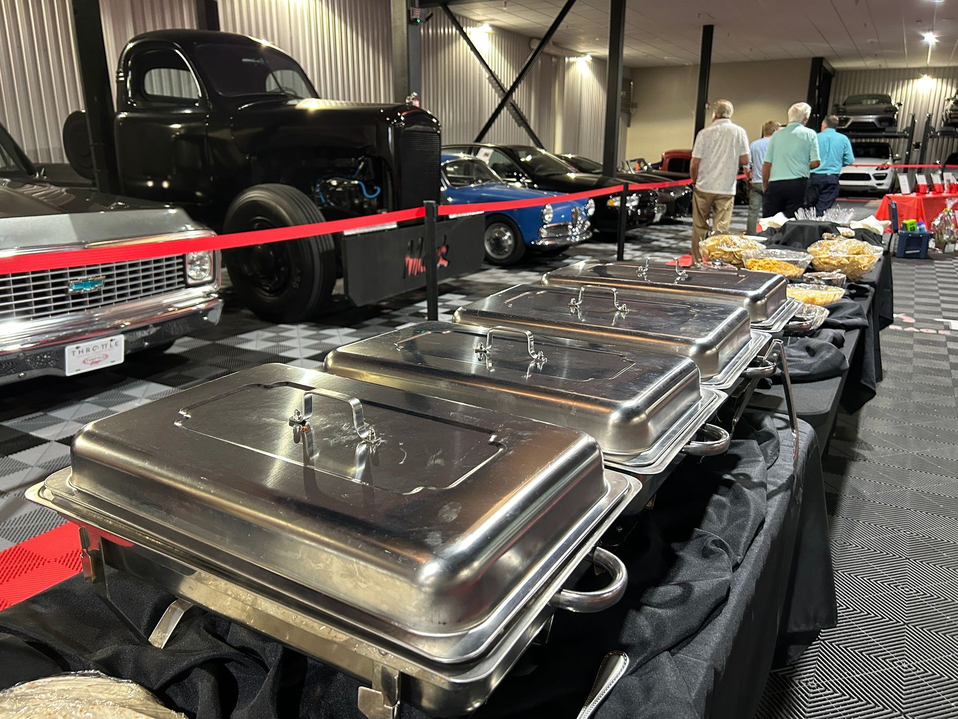 A row of stainless steel buffet trays in a room with cars in the background.