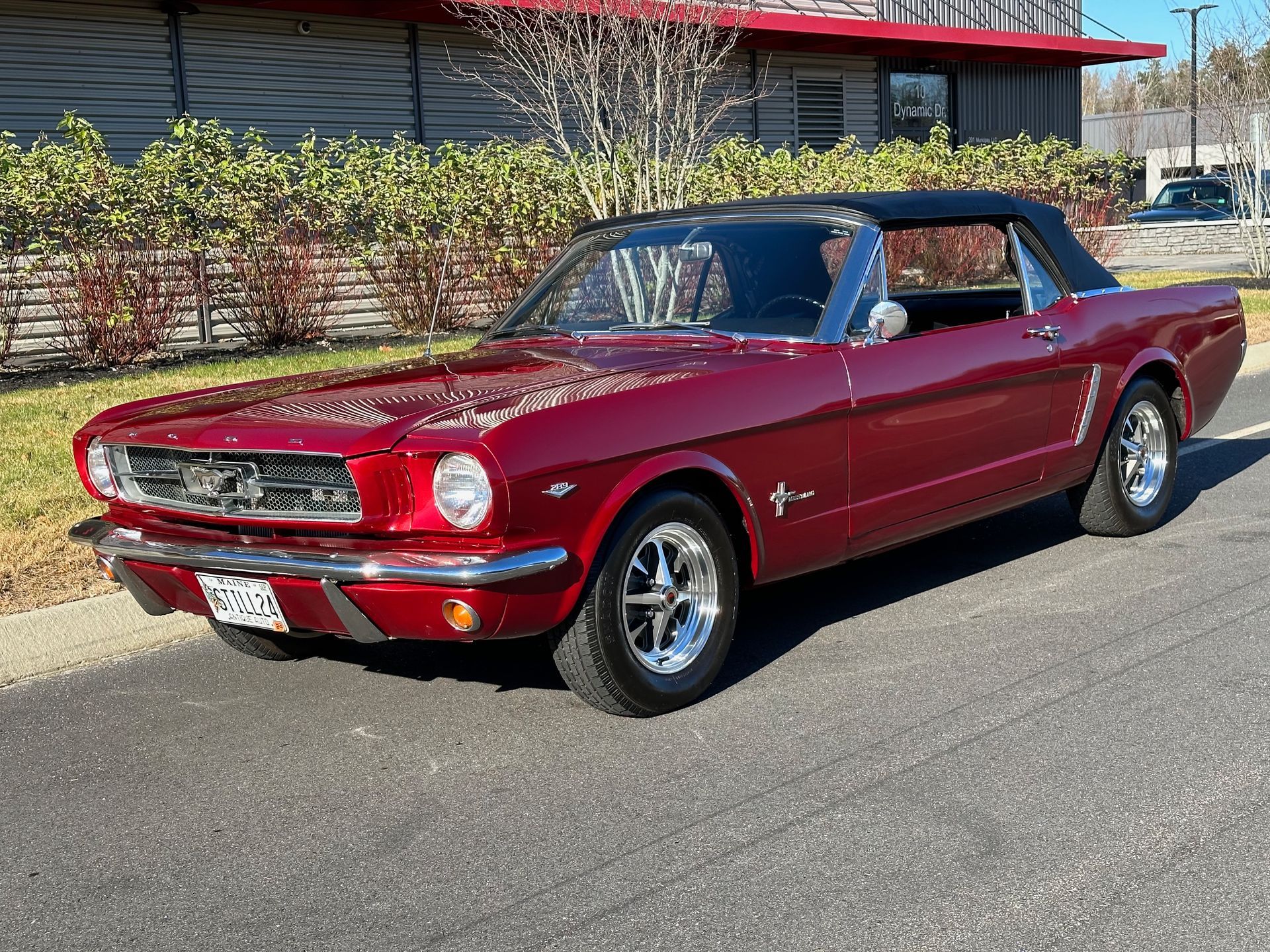 A red mustang is parked on the side of the road in front of a building.