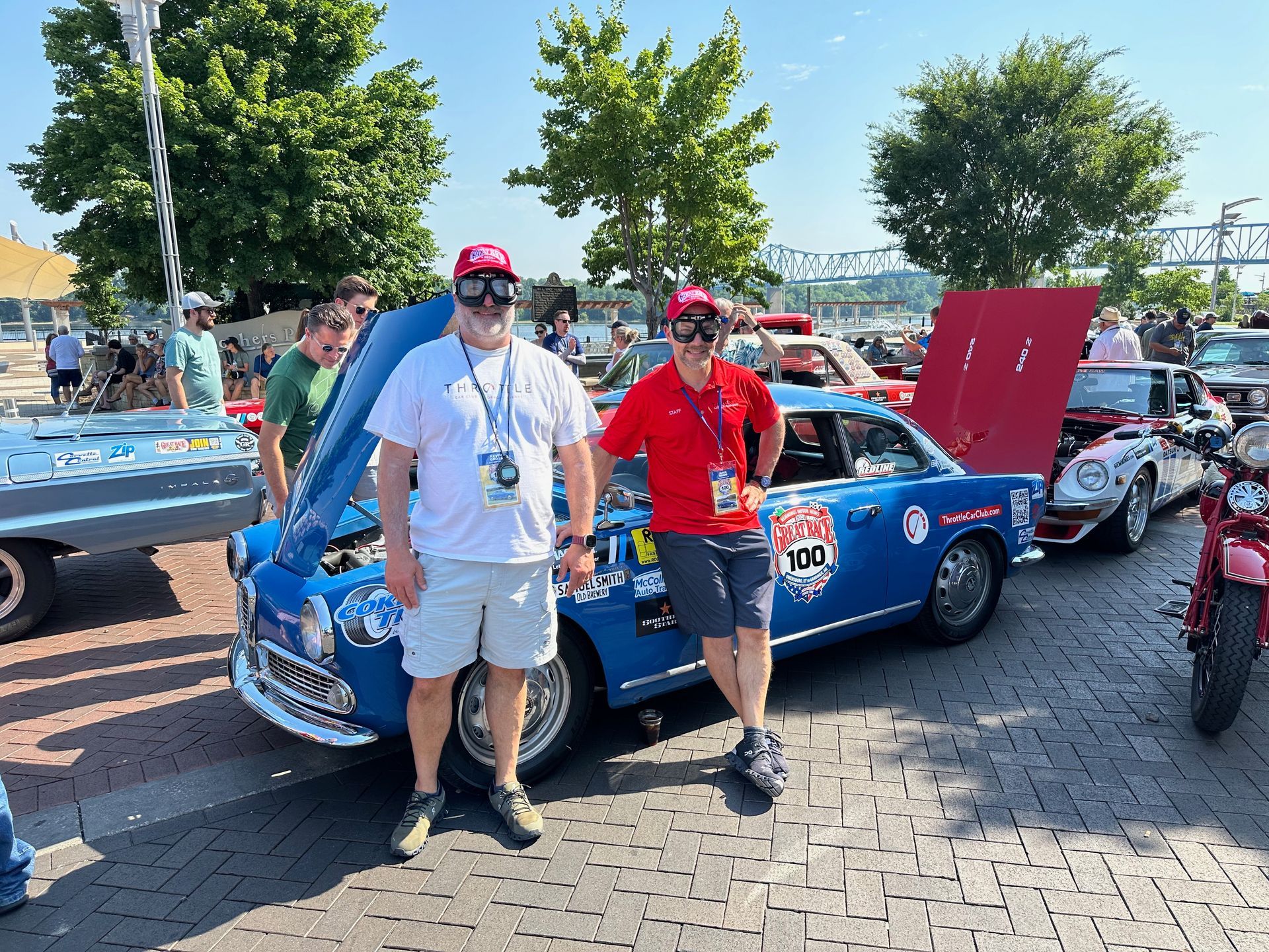 Two men are standing in front of a blue car with the hood up