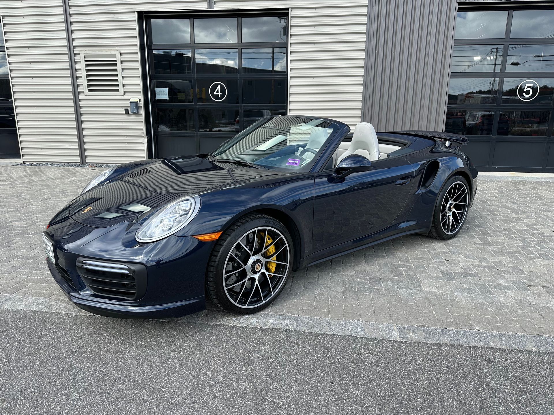 A blue porsche 911 turbo s convertible is parked in front of a garage.