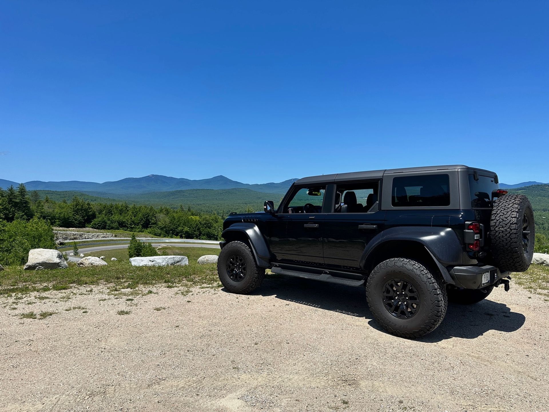 A black jeep is parked on a dirt road with mountains in the background.