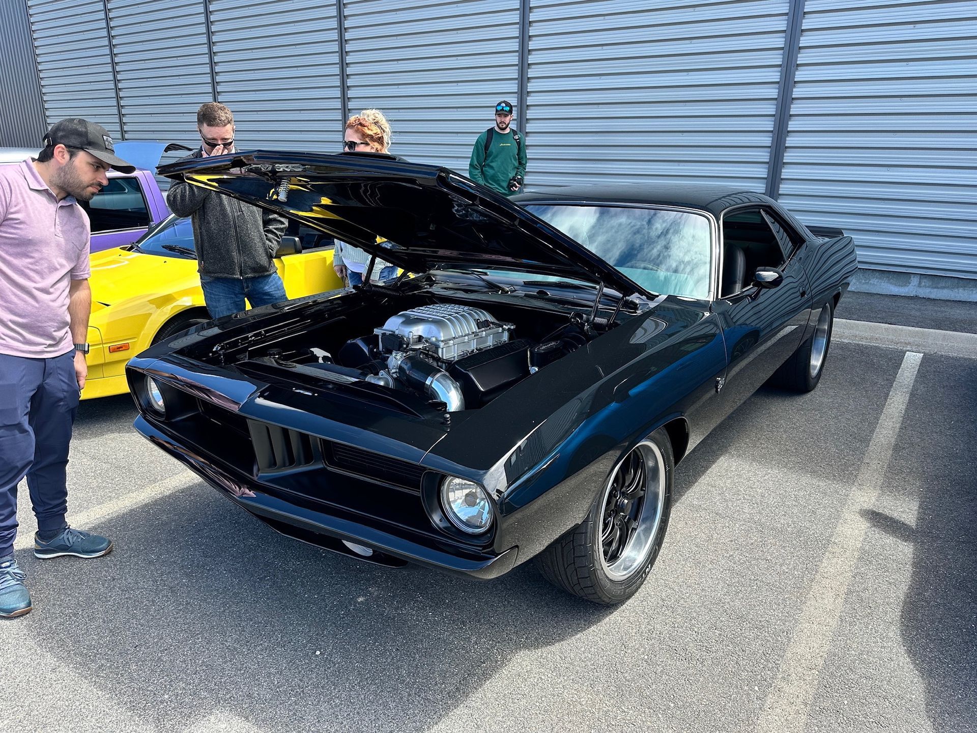 A black car with the hood up is parked in a parking lot.