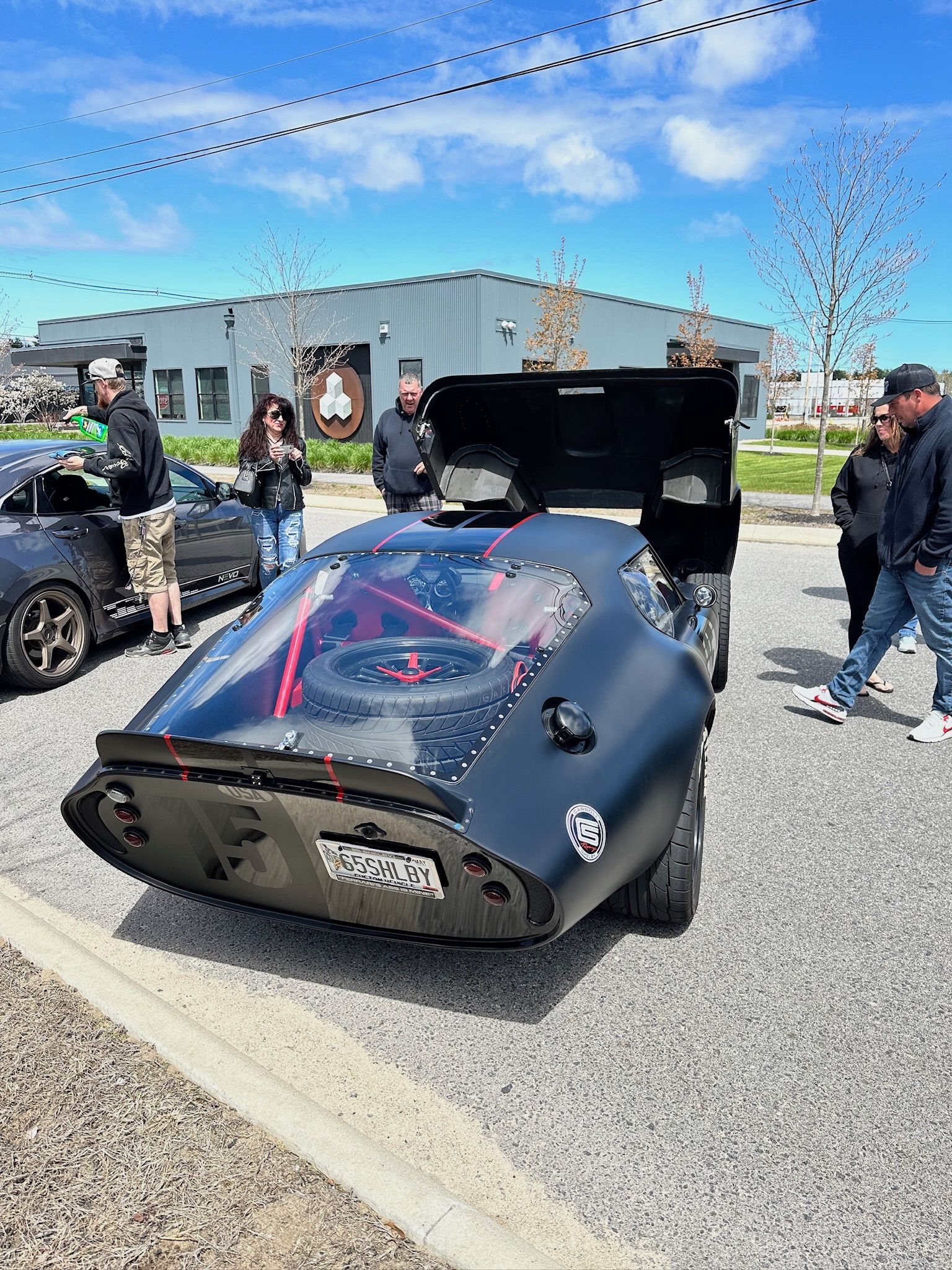A group of people are standing around a black car in a parking lot.