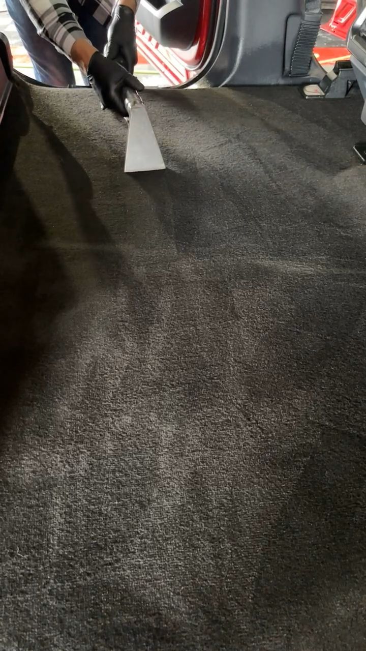 A person is cleaning the carpet of a car with a vacuum cleaner.