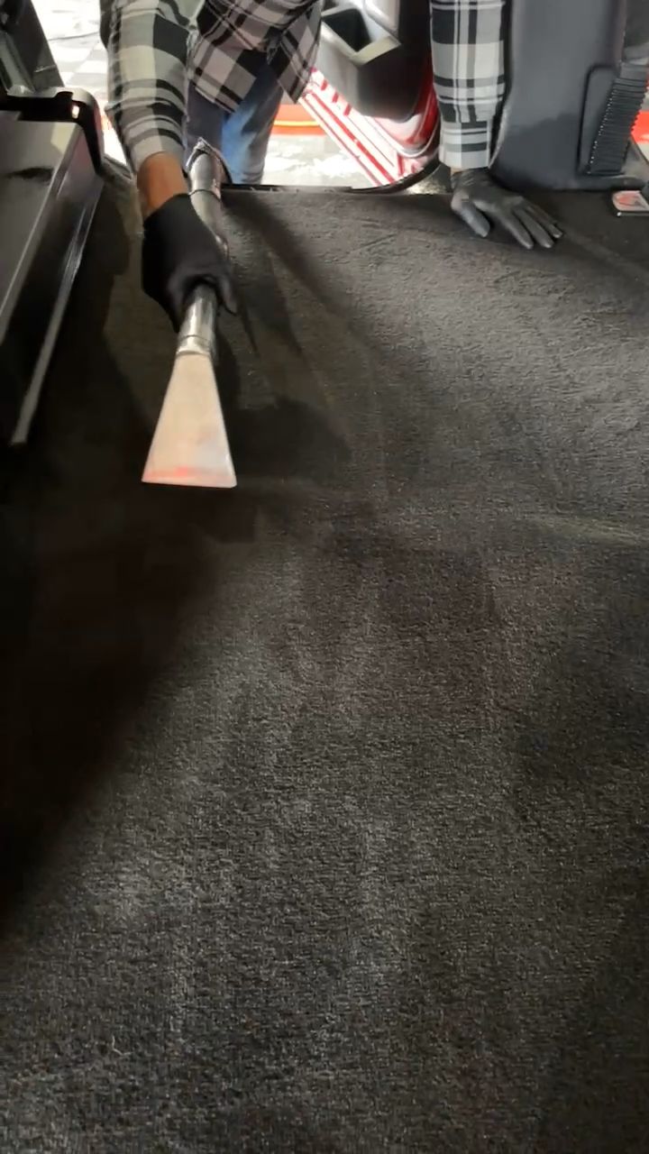 A person is using a vacuum cleaner to clean a carpet in a car.