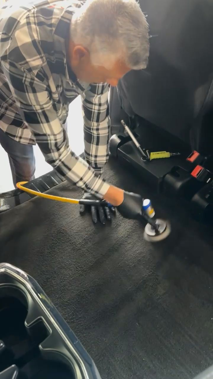 A man in a plaid shirt is cleaning the carpet of a car.