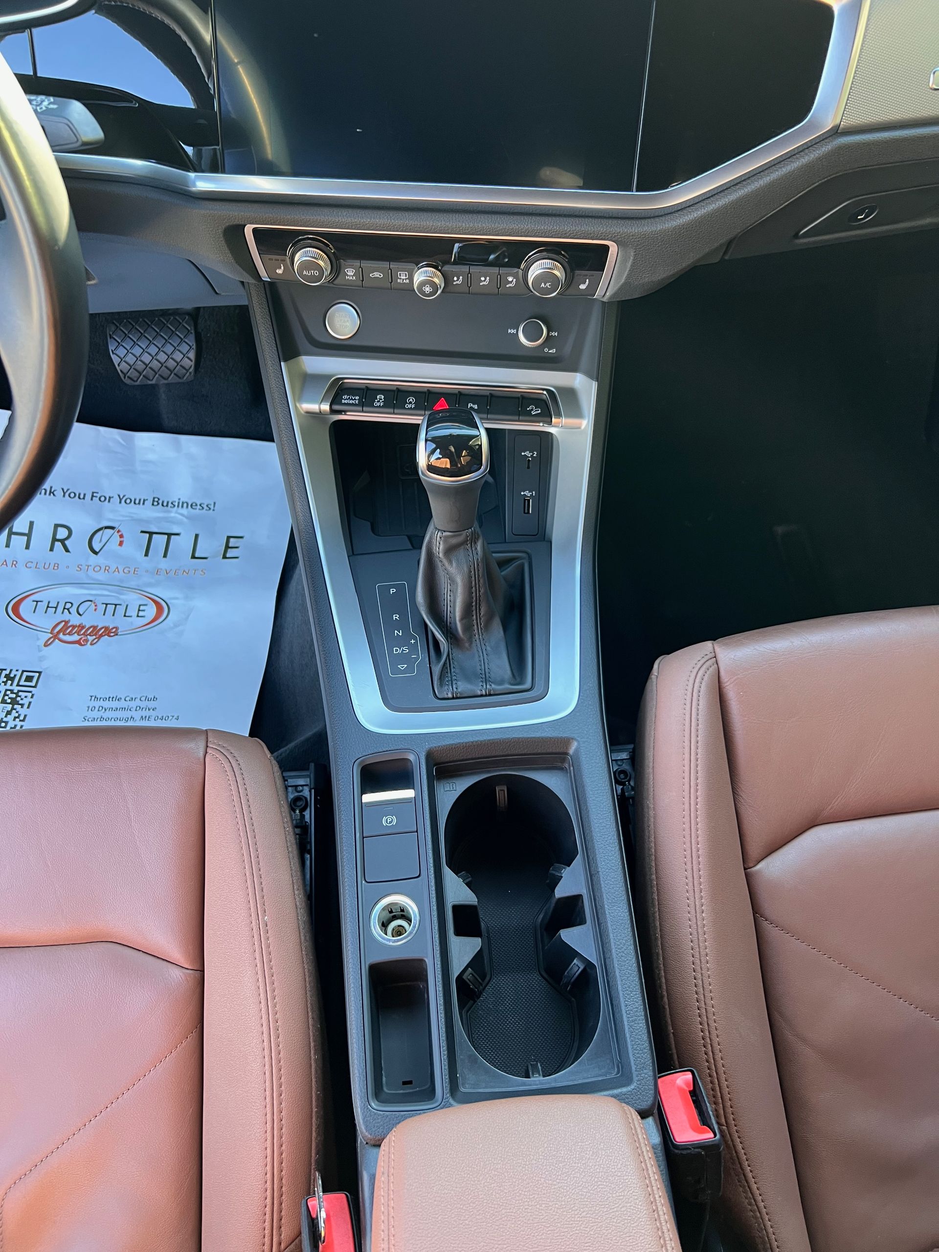 The interior of a car with brown leather seats and a cup holder.