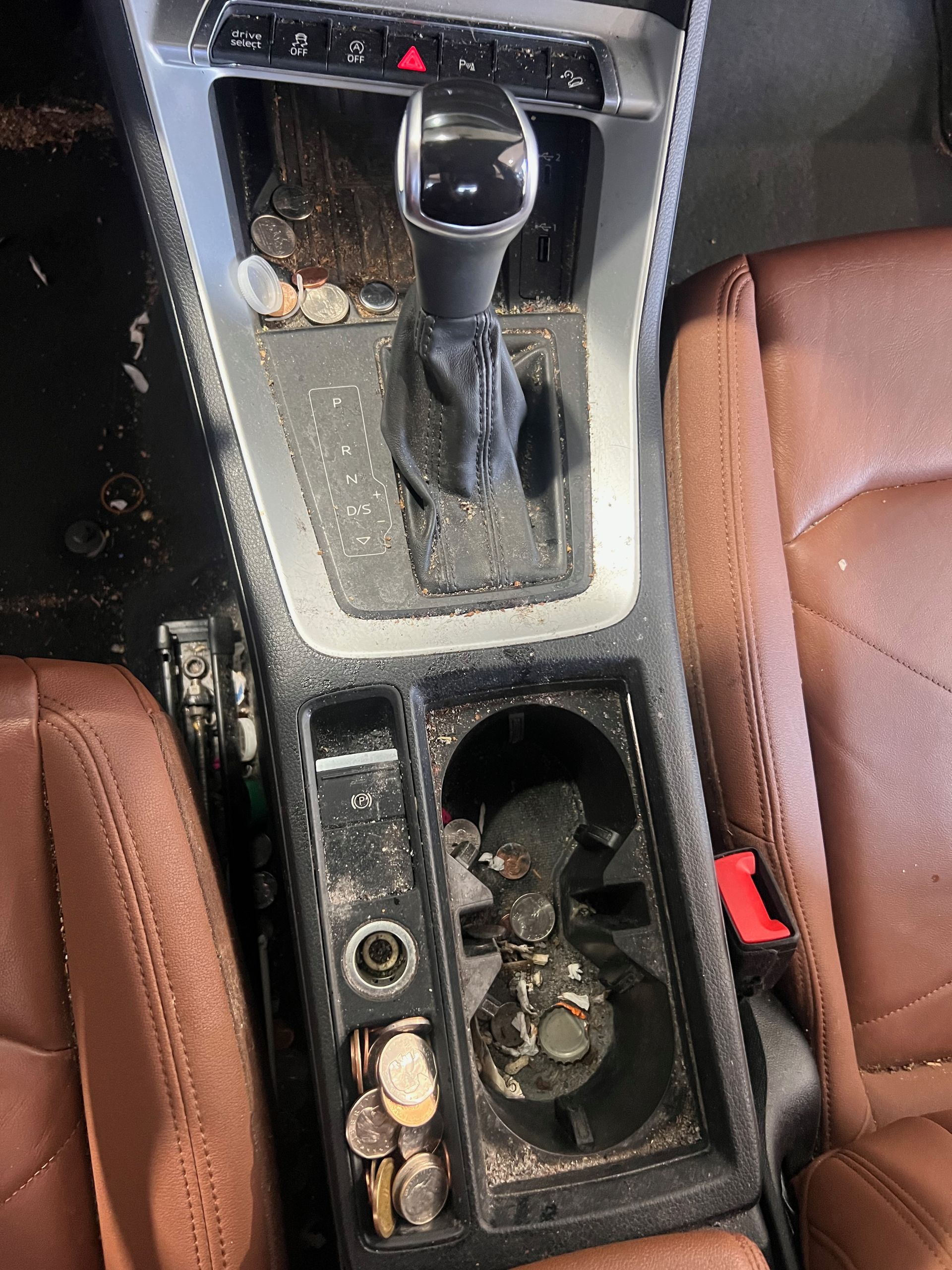 A dirty car console with a cup holder and coins in it.