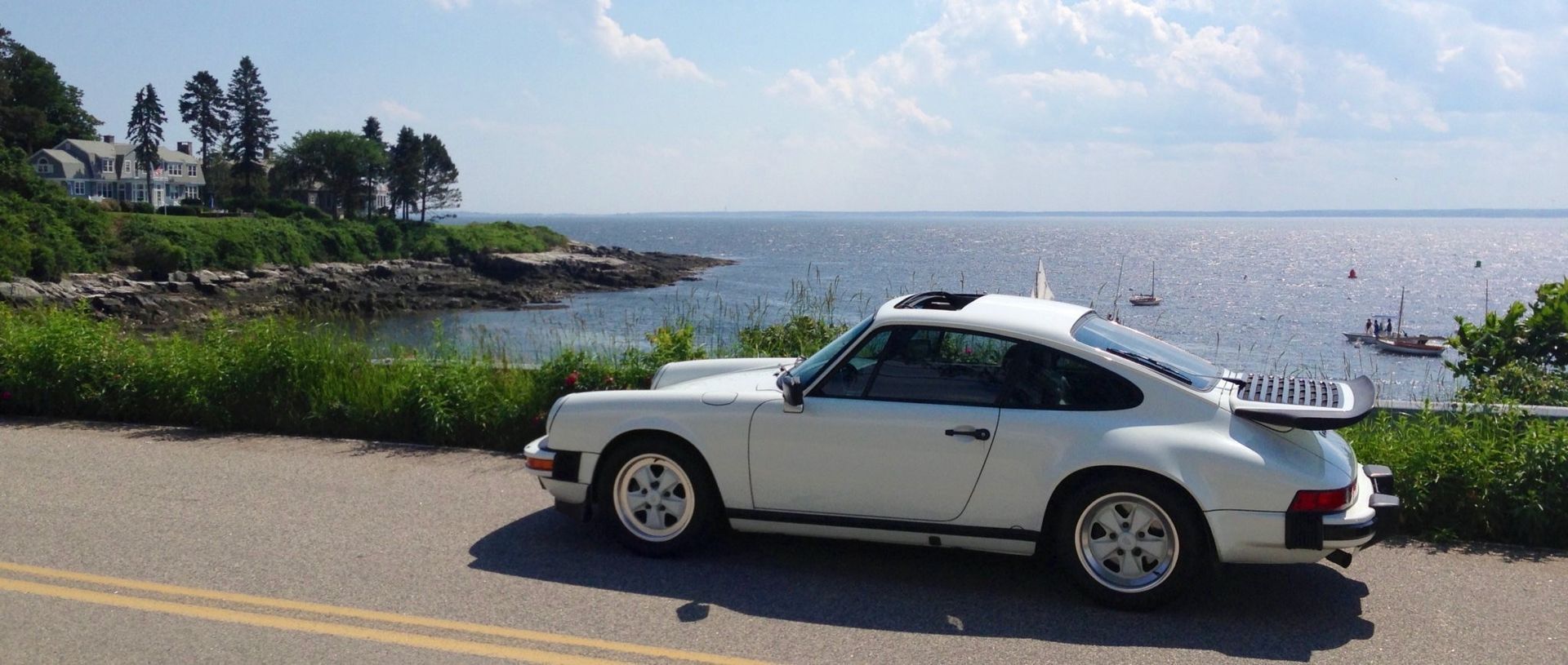 A white car is parked on the side of the road near the ocean