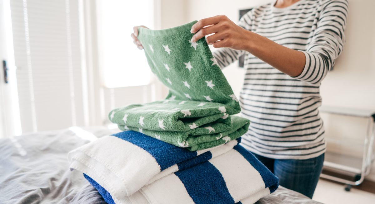 A woman is holding a green blanket over a pile of towels.