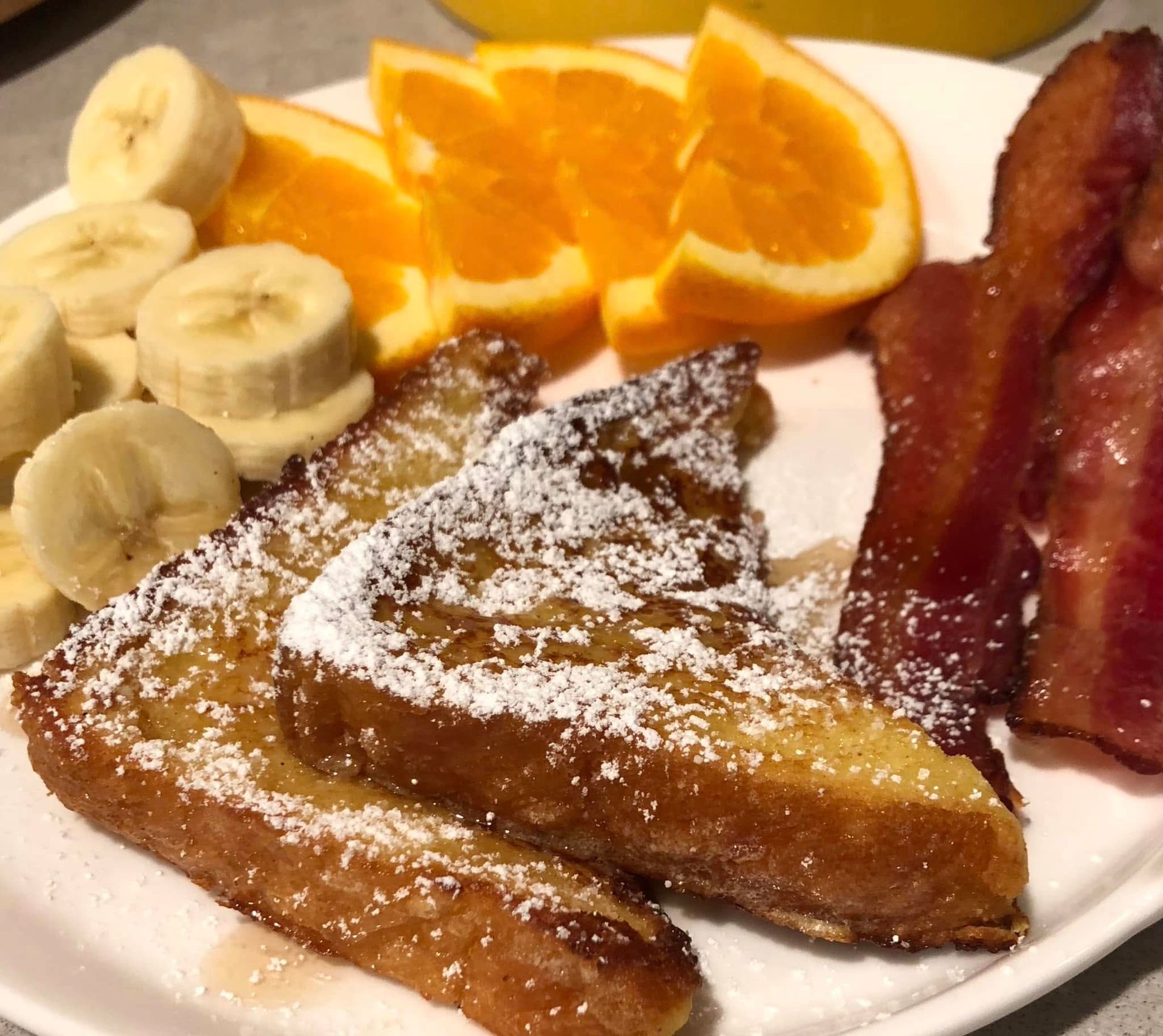 A white plate topped with french toast bananas and bacon