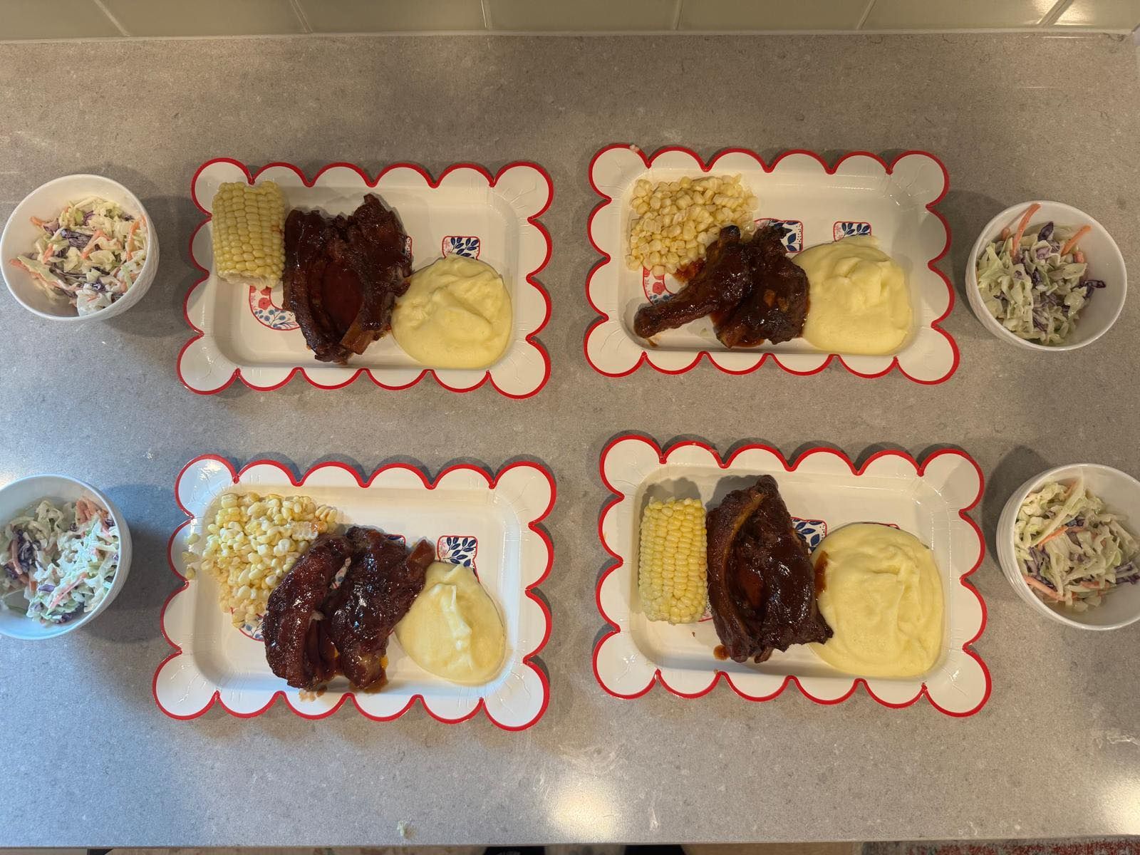 Four plates of food on a table with bowls of coleslaw and mashed potatoes.
