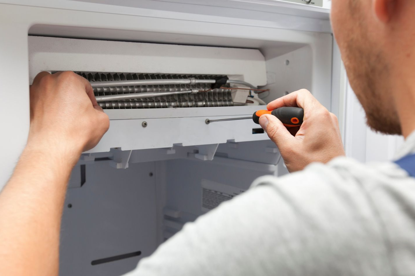 Person using a screwdriver to repair the inside of a white appliance.
