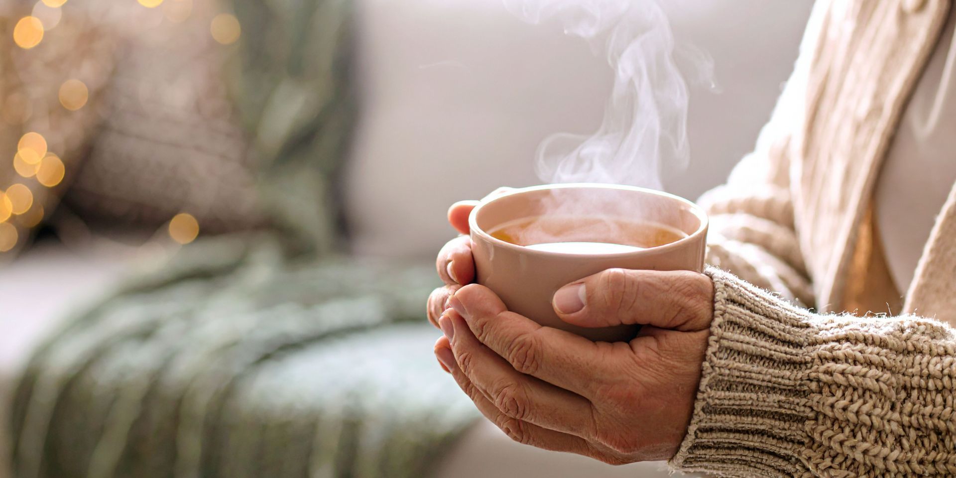 Person holding a warm, steaming cup of tea, cozy setting.