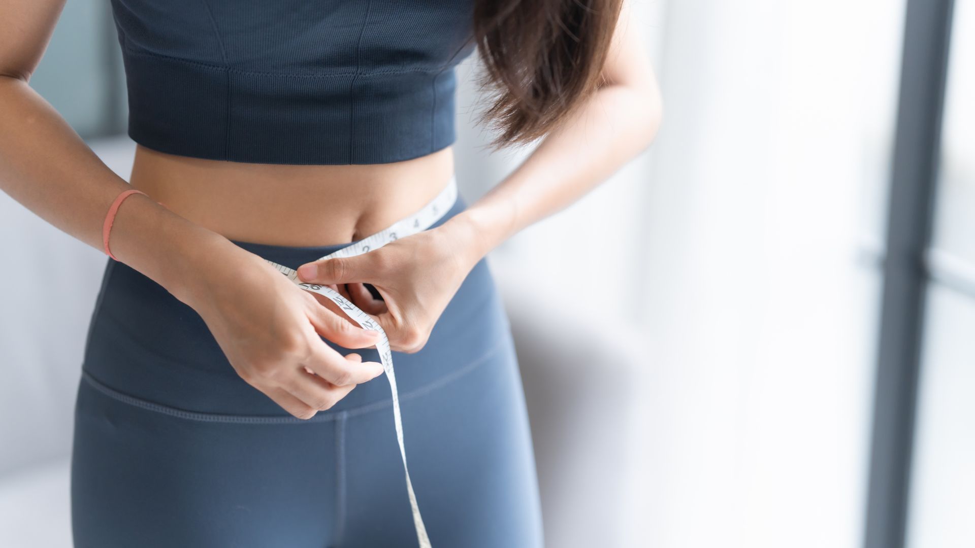 Person measuring waist with a tape measure while wearing dark workout clothes.