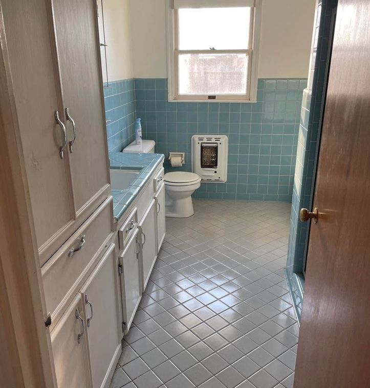 Narrow bathroom with blue tile, white sink and toilet, and a small window.