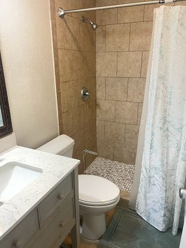 Small bathroom with toilet, vanity sink, tiled shower, and white curtain; pebble shower floor.