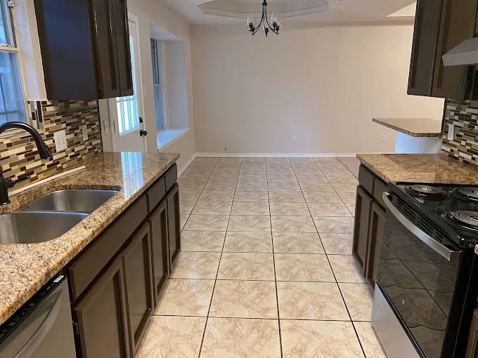 Empty kitchen with dark cabinets, granite countertops, tile floor, and a dining area beyond.