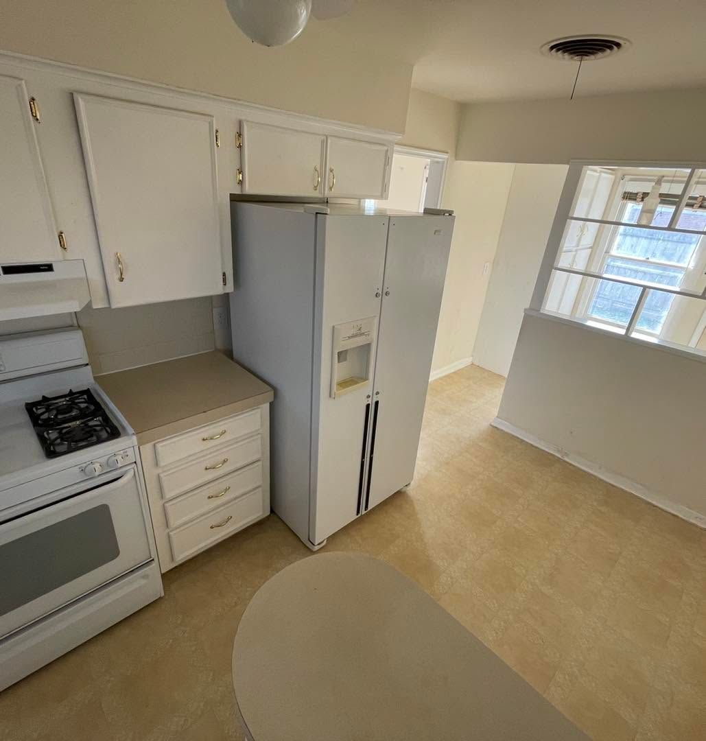 Small kitchen with white cabinets, stove, refrigerator, and a window on the right.