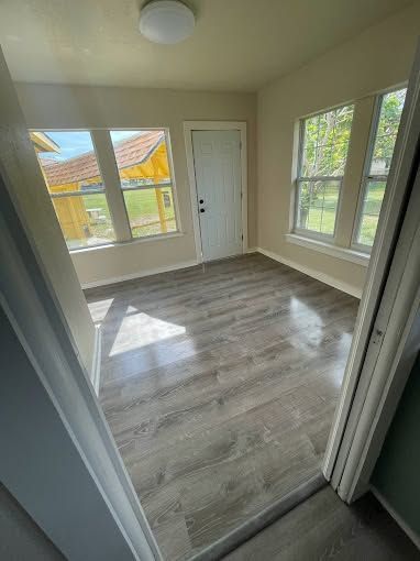 Empty beige room with gray wood-look flooring, white door, and large windows letting in sunlight