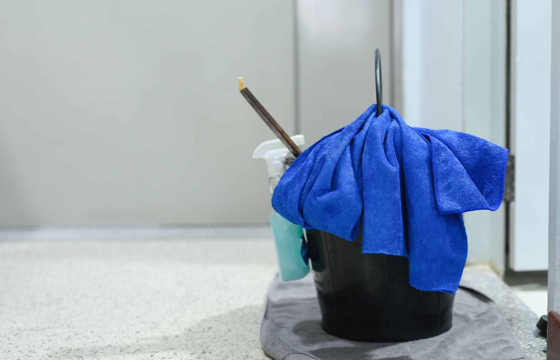 Blue cloth draped over a black bucket with cleaning brushes beside a wall