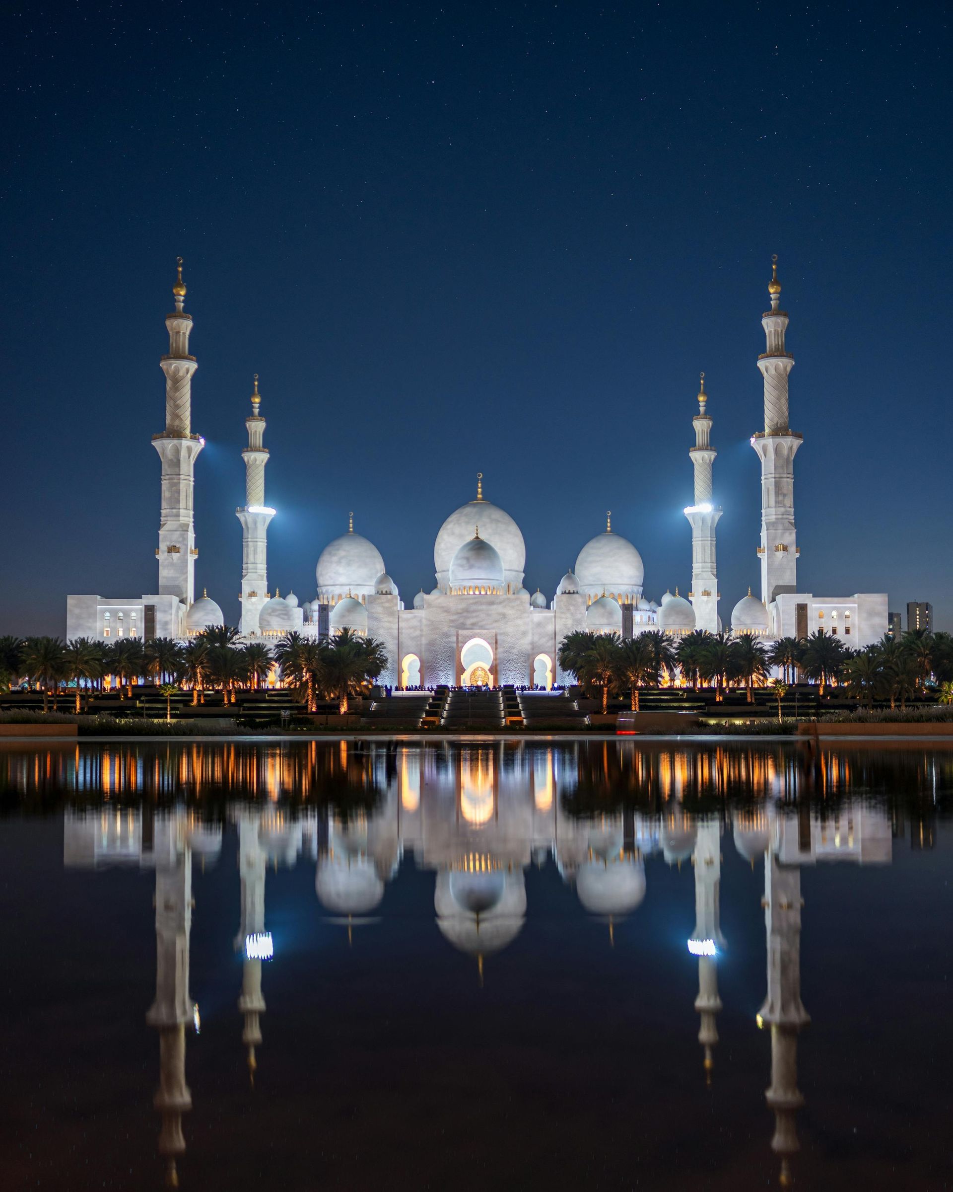 Sheikh Zayed Grand Mosque in Abu Dhabi illuminated at night with its reflection in the water, a 5-star Gulf destination ideal for premium First & Business Class Flight + Hotel packages - xLuxuryFlights.com