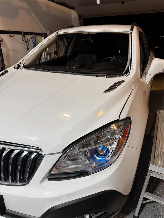 A white car with a missing windshield, parked inside a garage.