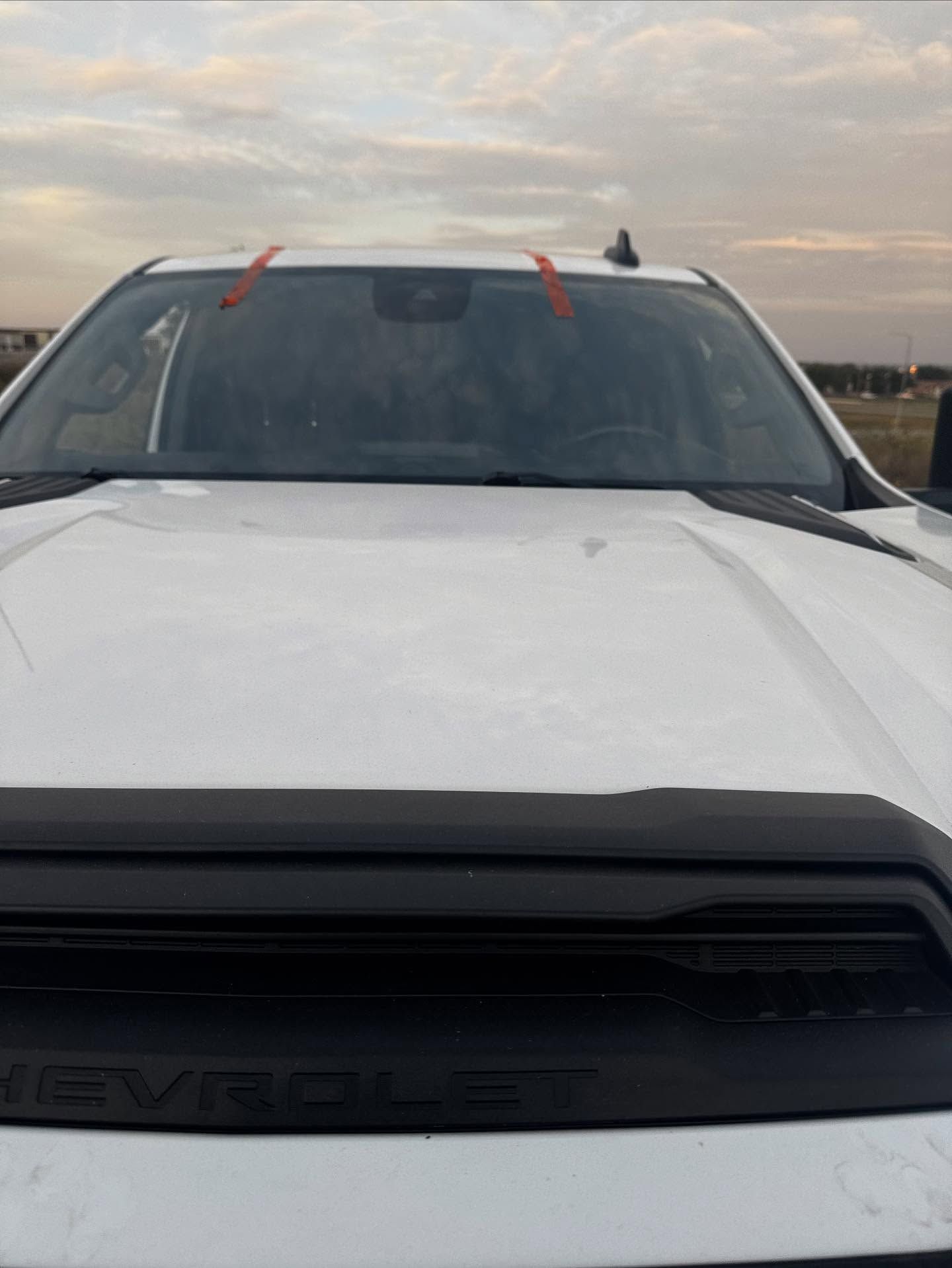 A front-facing view of a white Chevrolet truck with orange tape markers visible on the windshield.