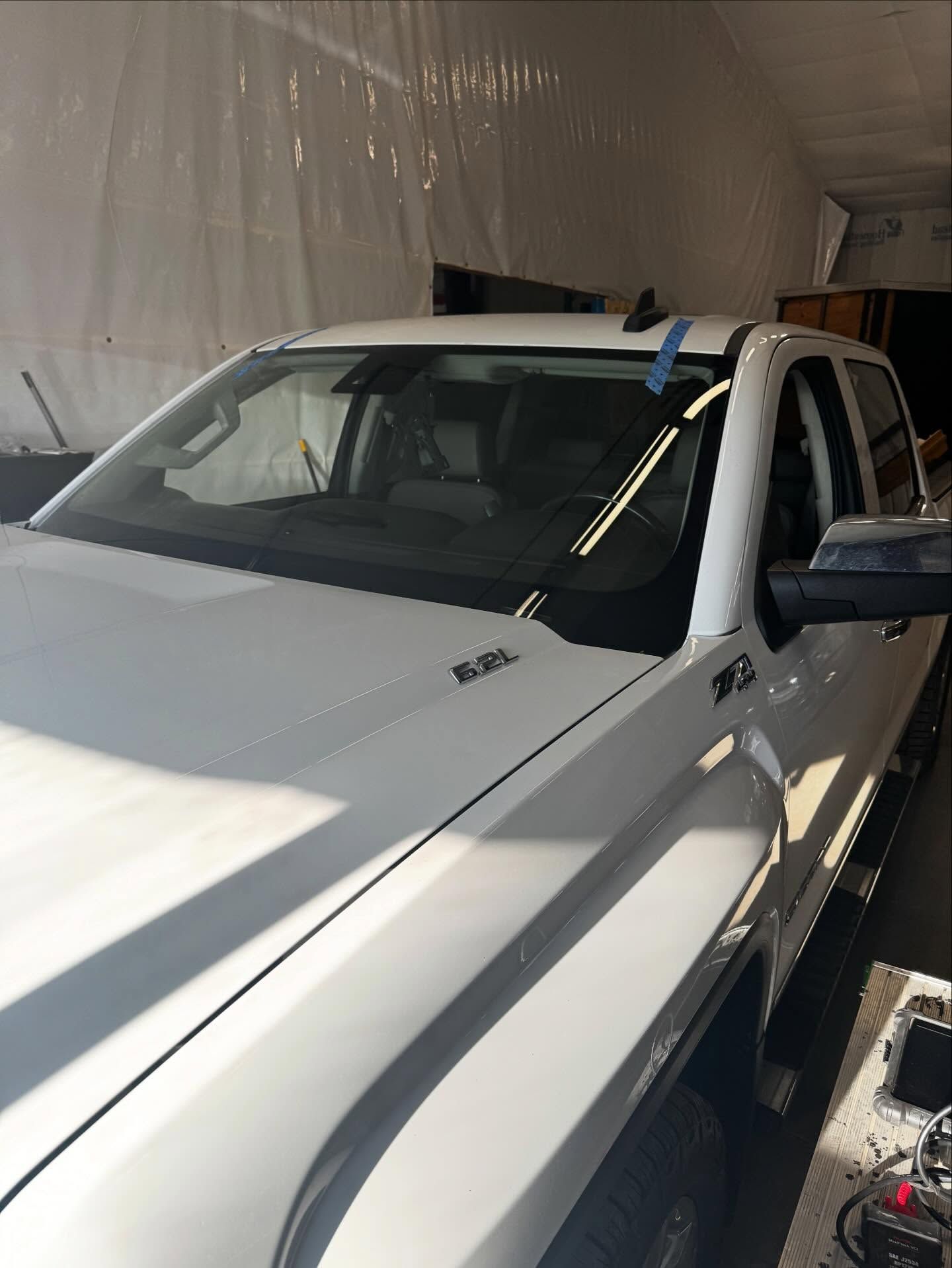 A white pickup truck parked indoors, featuring a 6.2L engine badge and blue masking tape on the windshield.