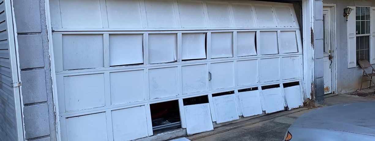 Damaged white garage door with broken panels and a low opening at the bottom