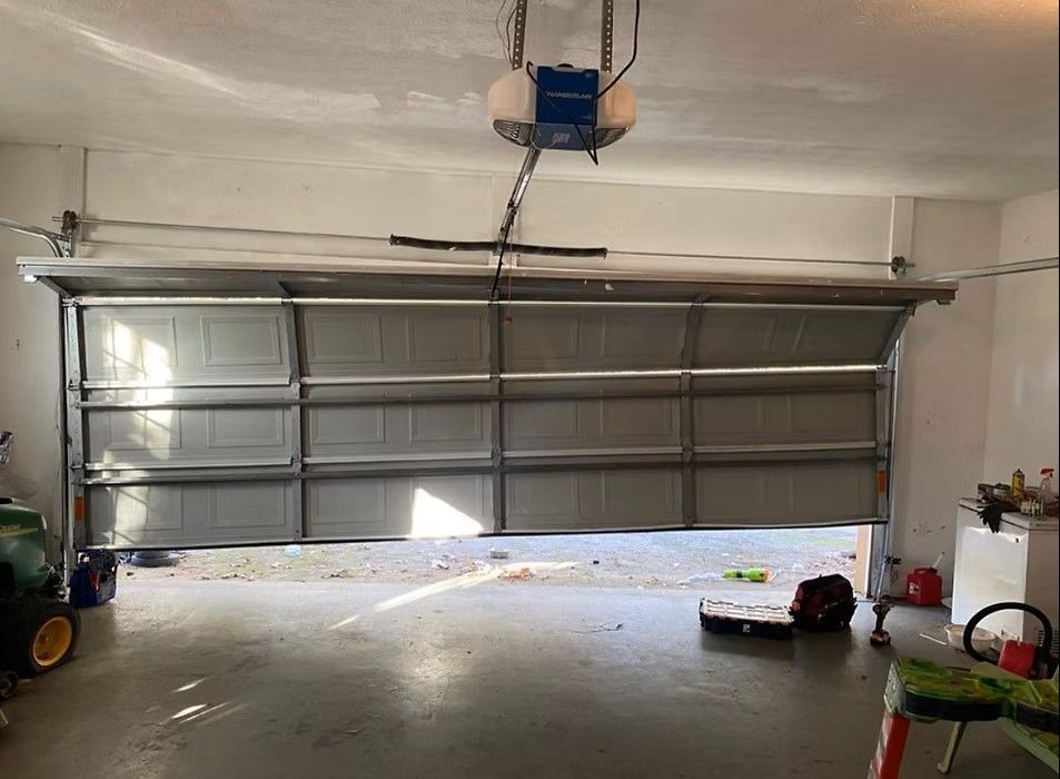 Garage interior with closed silver overhead door, concrete floor, and scattered tools and items.