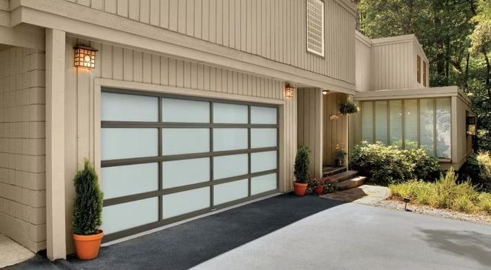 Modern beige house exterior with glass-pane garage door, potted plants, and a curved driveway