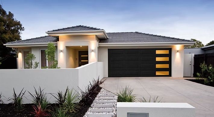 Modern single-story house with white walls, dark roof, and lit front entry at dusk