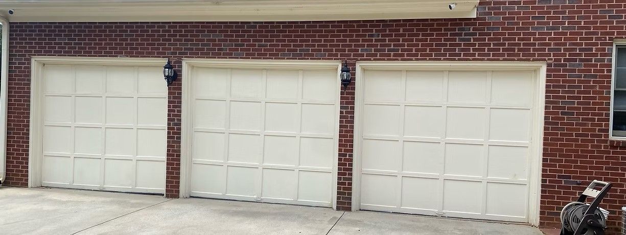 Three white garage doors set in a red brick building with a paved driveway in front