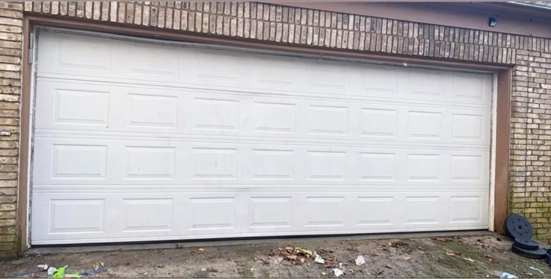 White double garage door on a brick house exterior, with a few items on the ground in front.