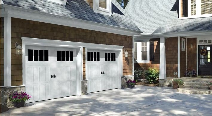 Two-car white garage doors on a stone house with a front porch and landscaped driveway