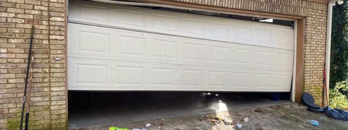 White garage door partially open with a small dog sitting in the driveway beneath it.